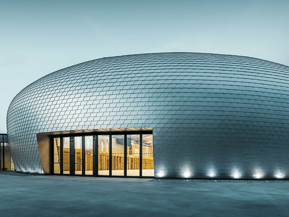 Die Sporthalle in Tschechien erinnert in ihrer Form an ein UFO - dazu wurden 20.000 PREFA Wandschindeln in Naturblank verlegt