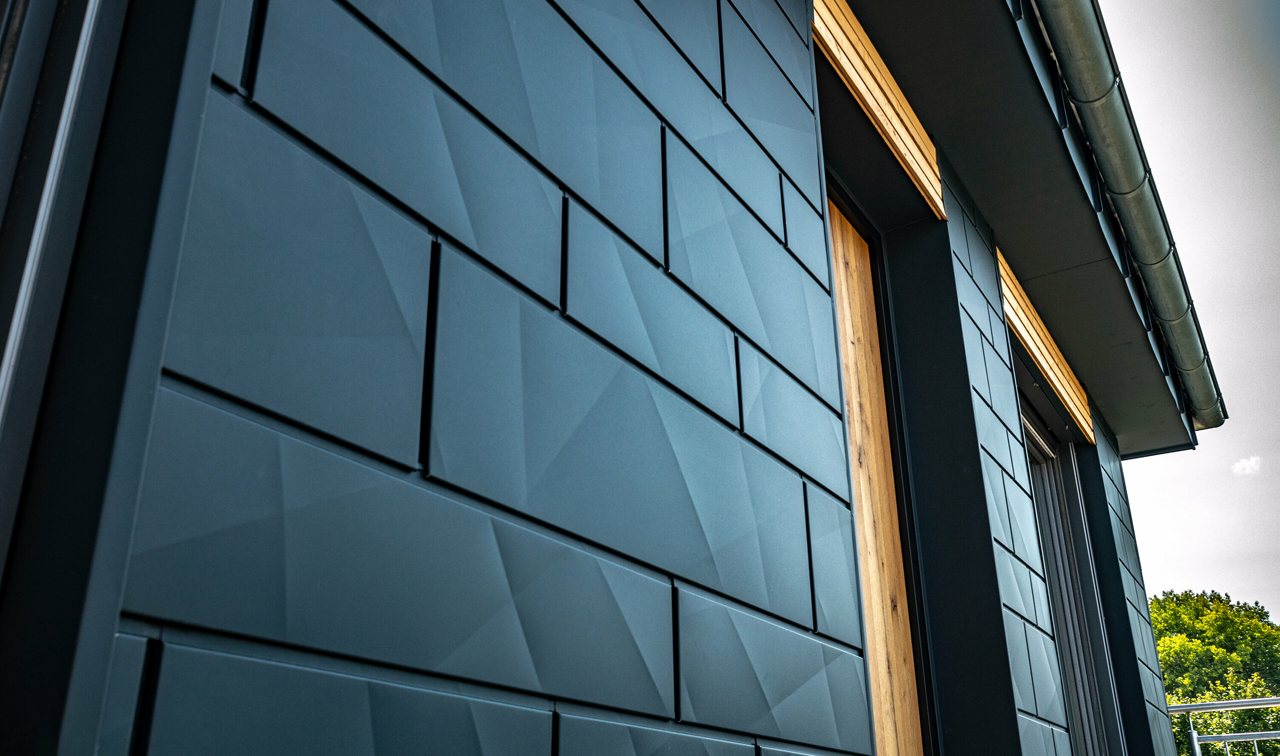 Fasáda s PREFA Siding.X v antracitové barvě. Boční pohled na objekt s balkonovými dveřmi a velkými prosklenými plochami v kombinaci s dřevěnou fasádou.