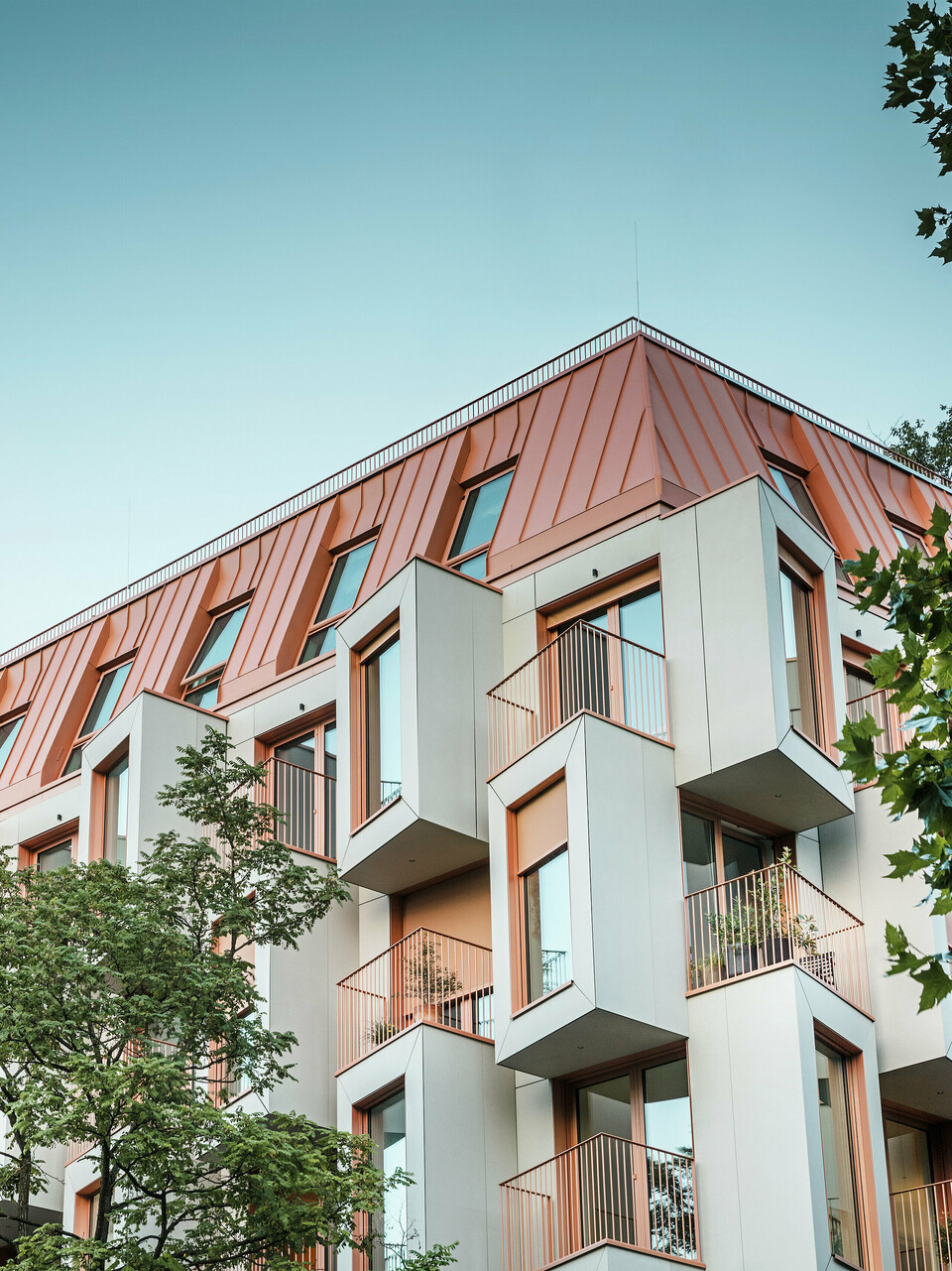Moderní rezidenční architektura v projektu Van B v Mnichově s inovativní fasádou s arkýřovými okny a výraznou hliníkovou střechou PREFALZ ve speciální barvě IGP Orange HDP od společnosti PREFA. Vysoce kvalitní střešní materiál zaujme svou extrémní trvanlivostí, vysokou odolností a stálostí barev. V kombinaci s kubickým designem fasády a velkými okenními plochami vzniká harmonický celkový obraz, který kombinuje funkčnost, design a udržitelnost na nejvyšší úrovni – ideální pro městský život.