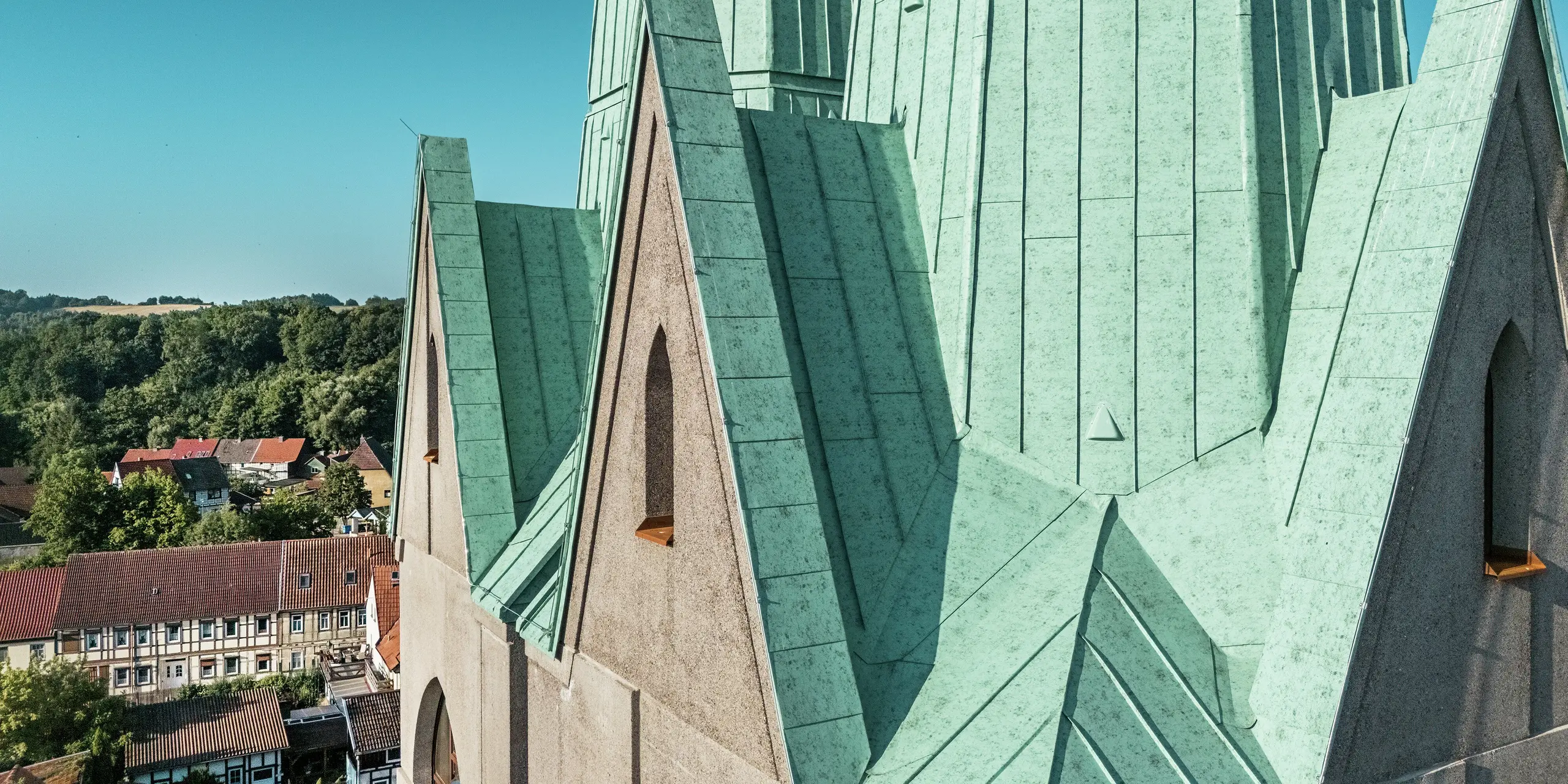 etailaufnahme des neu errichteten Kirchturms des Tourismuszentrums Ellrich: Die präzise ausgeführten Falzlinien aus PREFALZ Aluminium in der Farbe P.10 Patinagrün ziehen alle Blicke auf sich. Die Oberfläche schimmert im Sonnenlicht und unterstreicht die moderne Interpretation historischer Architektur. PREFALZ ist robust, langlebig, wartungsarm und aufgrund seiner flexiblen Verarbeitungsmöglichkeiten perfekt für anspruchsvolle Dachgeometrien geeignet.