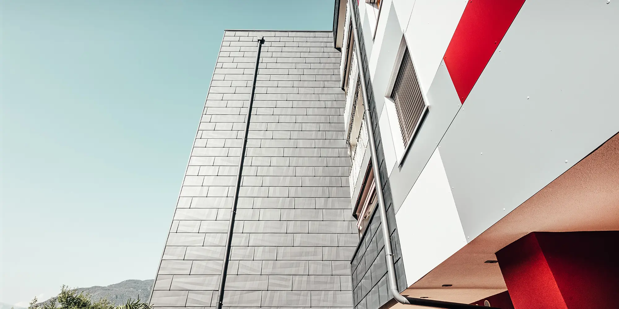 [Translate to česky:] Nahaufnahme von unten. Frontal: die anthrazitfarbene PREFA Fassade. Rechts: die weiß-grau-rote Fassadenfront.