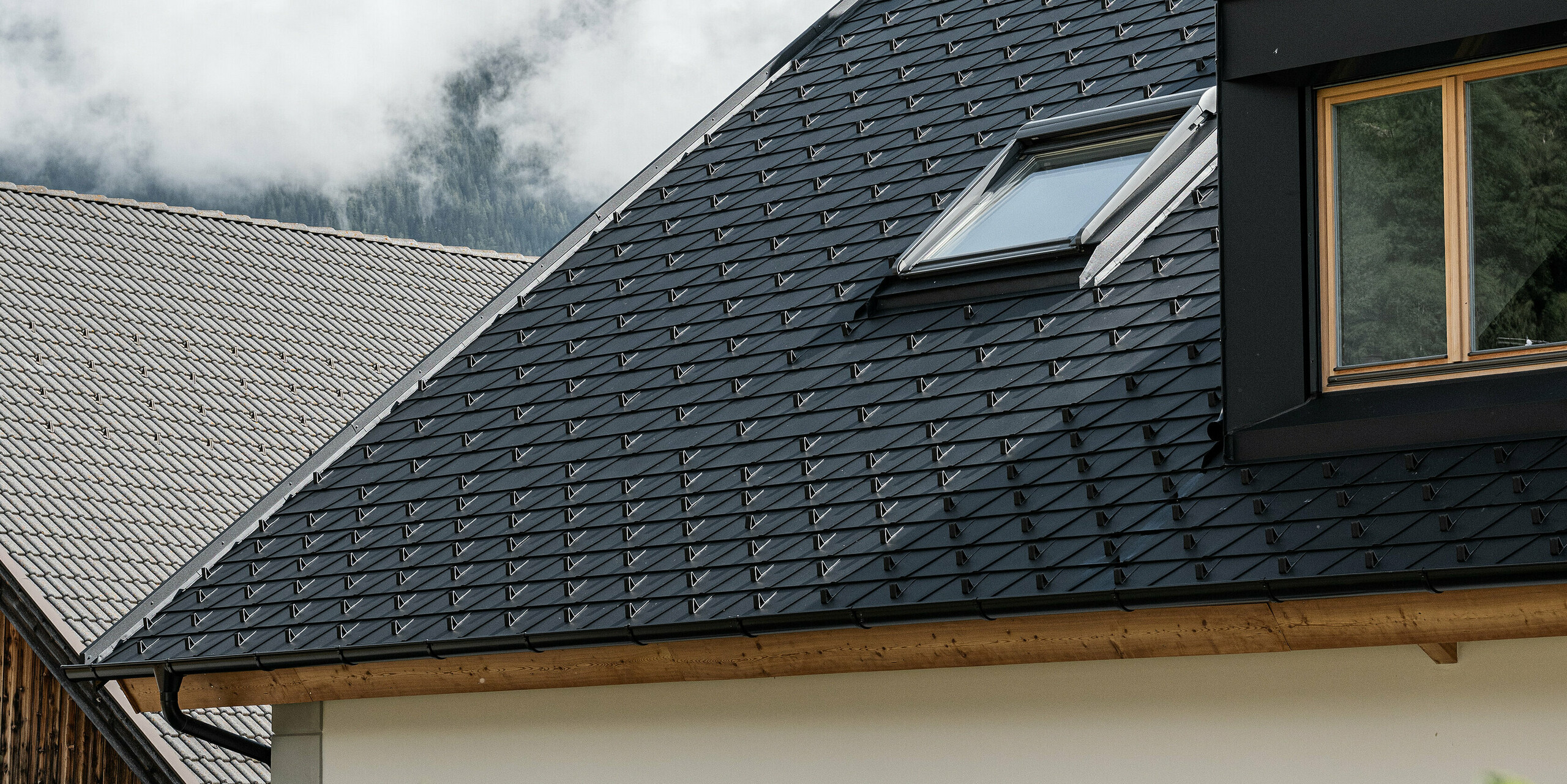 Detailní pohled na střešní systém PREFA odolný proti vichřici a povětrnostním vlivům. Sedlová střecha Ausserwegerhof v Jižním Tyrolsku byla vybavena robustními střešními šindely PREAF DS.19 v barvě P.10 antracit. Estetické řešení střechy je obklopeno působivou horskou kulisou údolí Antholz.