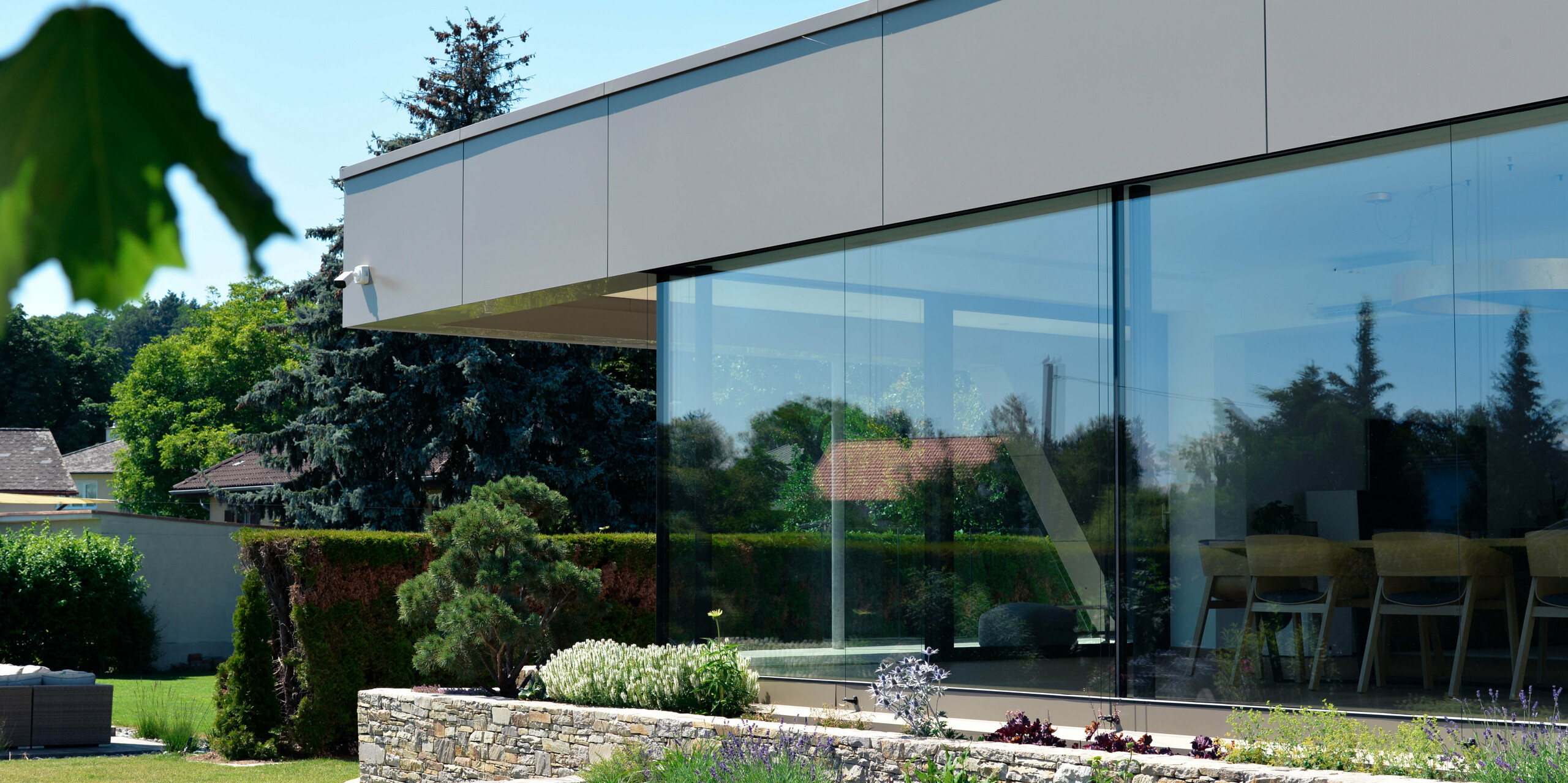 Blick aus dem Gebüsch auf die Terrasse verkleidet mit PREFA Aluminium Verbundplatten in Bronze