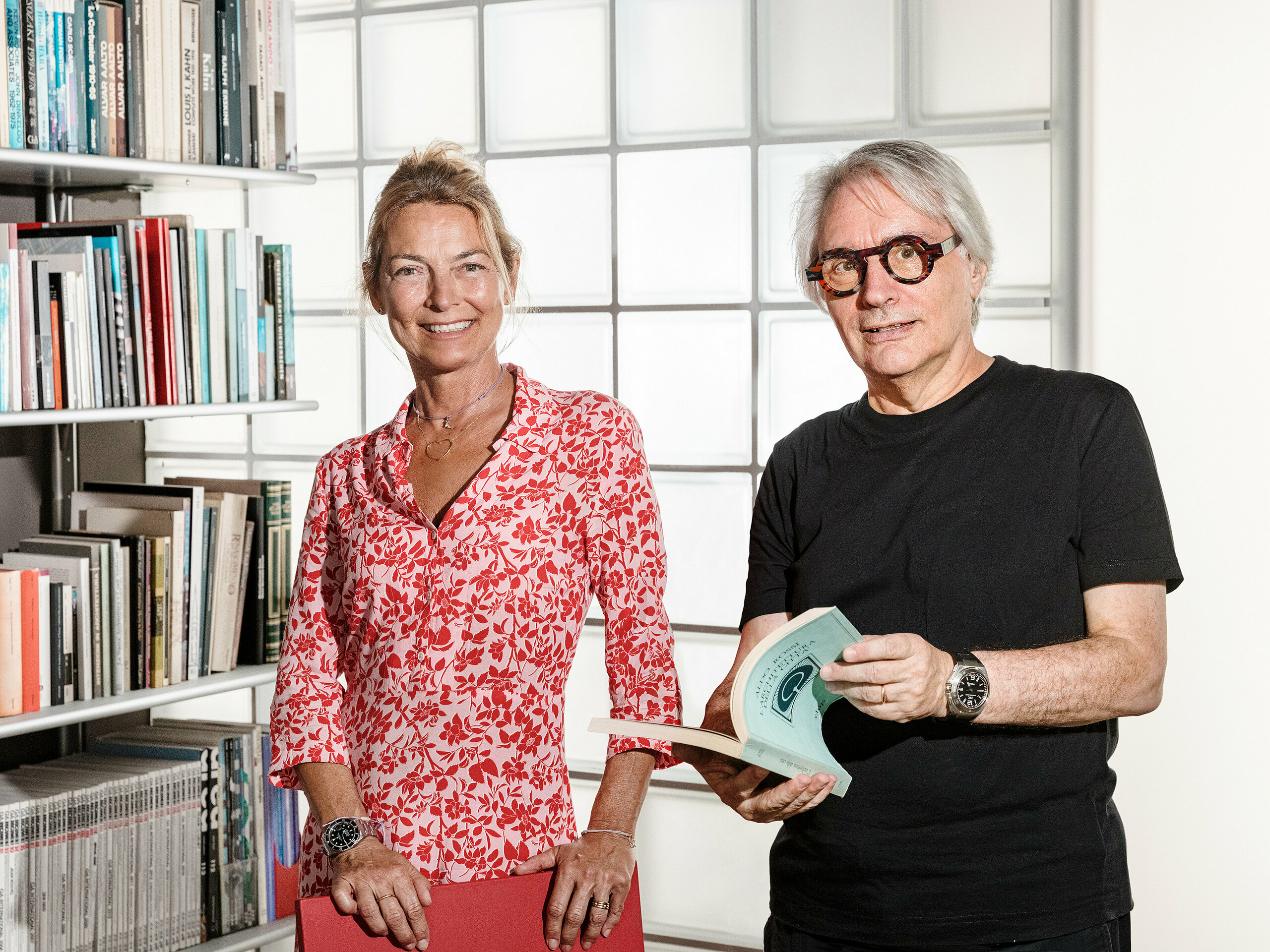 Bolzanský architekt Claudio Lucchin a jeho partnerka Daniela Varnier pózují před moderní skleněnou cihlovou zdí, která vzrušujícím způsobem láme světlo. Claudio Lucchin je oblečen celý v černém a drží knihu. Daniela Varnier má na sobě zářivě červený top a vřele se usmívá. Toto stylové prostředí symbolizuje inovaci a transparentnost. Scéna představuje průkopnickou architekturu, jaká se projevila v kasárnách „Tempesti“ v Corvaře v Jižním Tyrolsku.