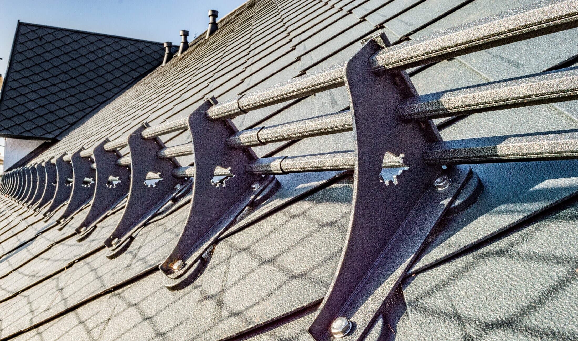Detail protisněhového prvku - svěrka profilované trubkové zábrany s trubkou sněhové zábrany na střeše s falcovanou šablonou 29 x 29 v barvě P.10 antracitové na Hotelu Burg Maienluft.
