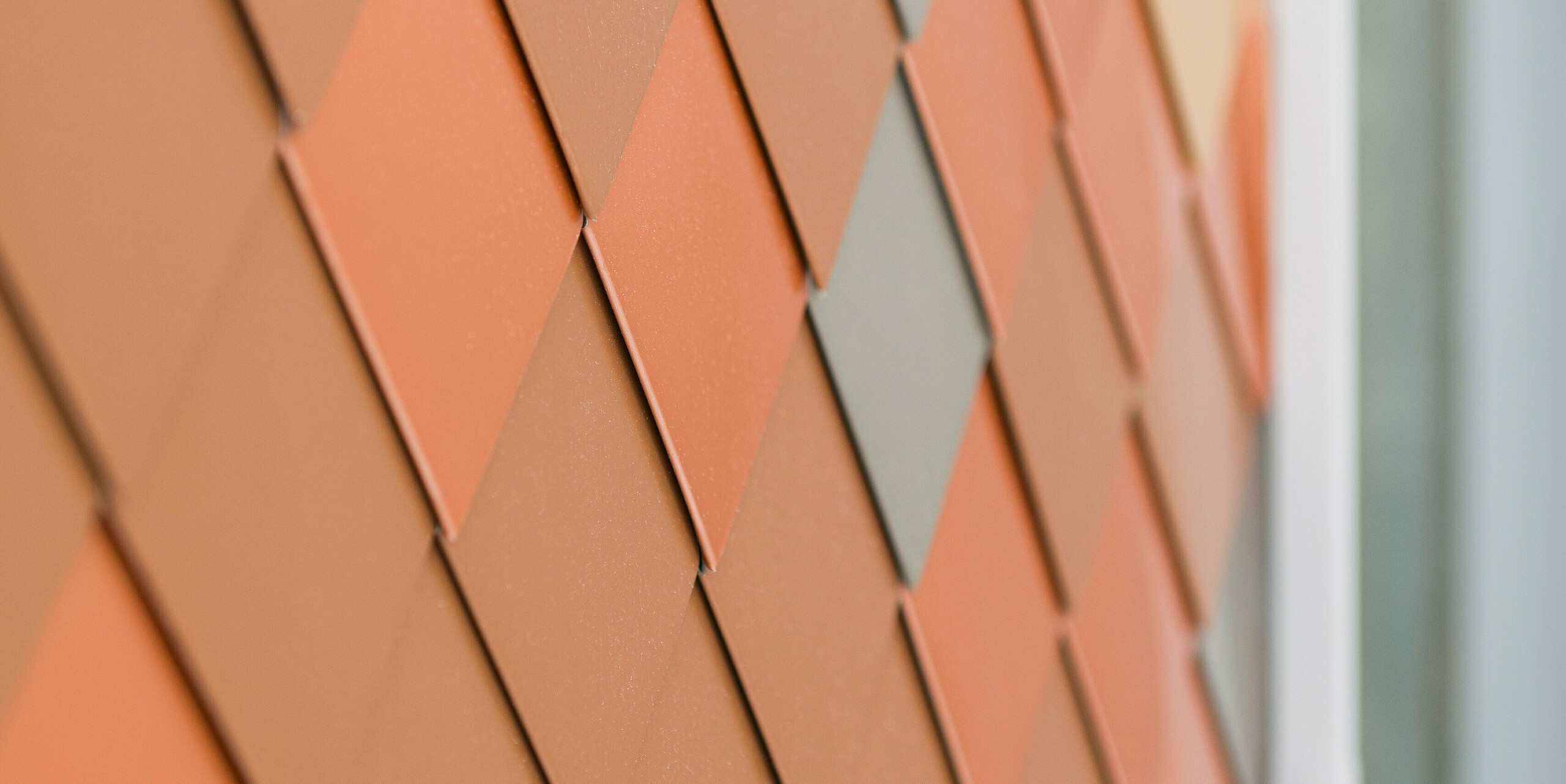 Detailní pohled na moderní hliníkovou fasádu PREFA s geometrickým vzorem v různých odstínech. Malé hliníkové fasádní šablony vytváří trojrozměrný vzhled, který zdůrazňuje strukturu a barevnou hloubku