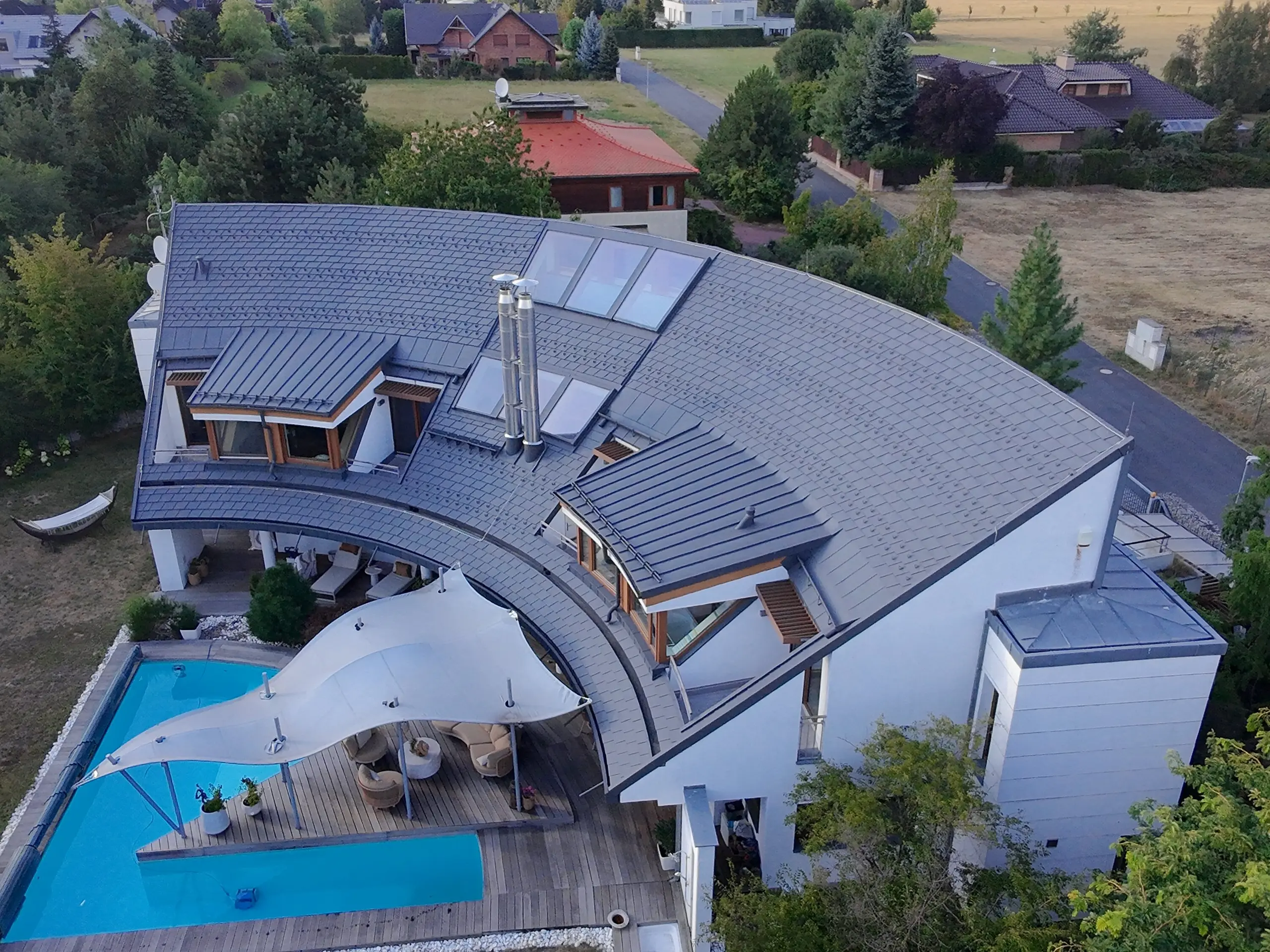 Pohled z dronu na nově zrekonstruovanou střechu s materiály PREFA - falcovanými šindeli a drážkovou krytinou PREFALZ v elegantní barvě P.10 tmavě šedé.