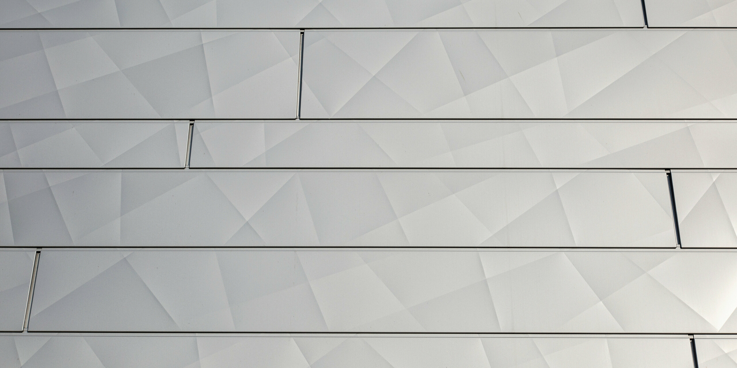 Detailní pohled na třpytivé fasádní panely PREFA Siding.X ve stříbrné metalíze v ploše s typickým optickými zlomy
