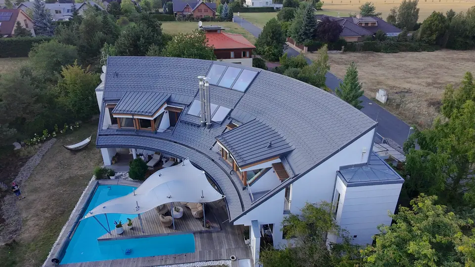 Pohled z dronu na nově zrekonstruovanou střechu s materiály PREFA - falcovanými šindeli a drážkovou krytinou PREFALZ v elegantní barvě P.10 tmavě šedé.