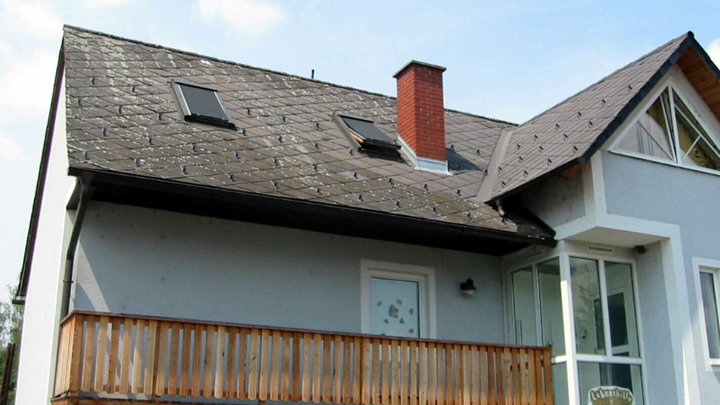 Rodinný dům se starou sedlovou střechou, cihlovým komínem a modrou fasádou připravený k sanaci střechy
