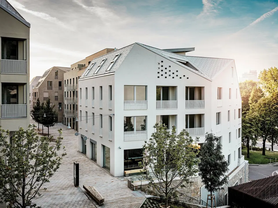 Moderní rezidenční čtvrť Vydrica v Bratislavě se vyznačuje čistým architektonickým stylem a klidnou uliční krajinou. Strmé sedlové střechy s výraznými světlíky jsou pokryty hliníkovými střešními šindeli PREFA v barvách P.10 Prefa bílá, bronzová a P.10 písková, které vytvářejí elegantní plochu na slunci. Precizně provedené linie a homogenní povrchy podtrhují vysoce kvalitní design. Hliník PREFA je známý svou trvanlivostí, nízkou hmotností a vysokou odolností vůči povětrnostním vlivům – ideální pro složité tvary střech a udržitelný, nenáročný plášť budovy.