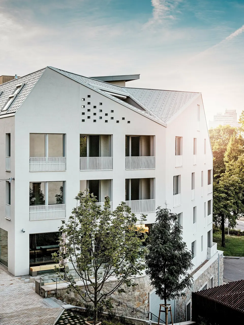 Moderní rezidenční čtvrť Vydrica v Bratislavě se vyznačuje čistým architektonickým stylem a klidnou uliční krajinou. Strmé sedlové střechy s výraznými světlíky jsou pokryty hliníkovými střešními šindeli PREFA v barvách P.10 Prefa bílá, bronzová a P.10 písková, které vytvářejí elegantní plochu na slunci. Precizně provedené linie a homogenní povrchy podtrhují vysoce kvalitní design. Hliník PREFA je známý svou trvanlivostí, nízkou hmotností a vysokou odolností vůči povětrnostním vlivům – ideální pro složité tvary střech a udržitelný, nenáročný plášť budovy.