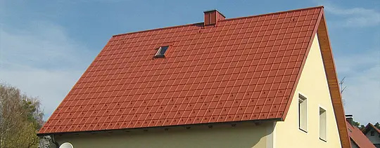 Klasická sedlová střecha s malým střešním oknem a komínem, pokrytá PREFA falcovanými střešními taškami v cihlově červené barvě včetně sněhových zarážek a střešních bezpečnostních háků.