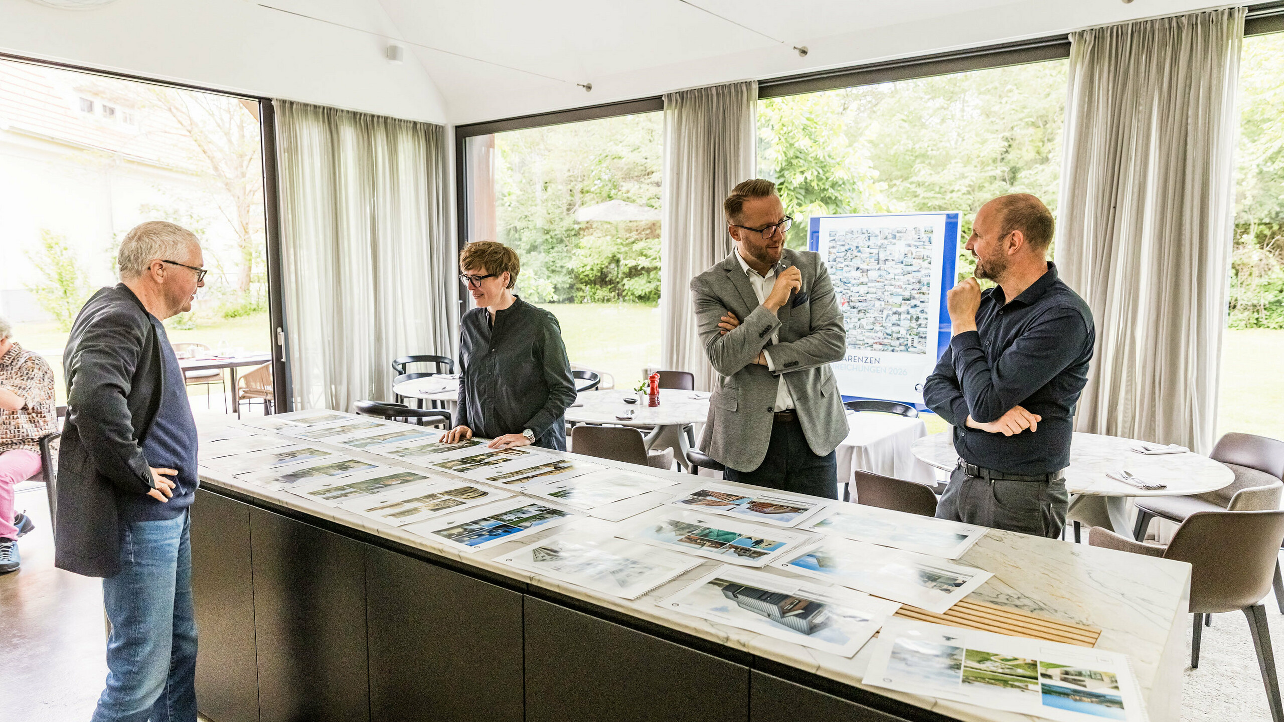 Konečný výběr architektonických vrcholů PREFARENZEN pro rok 2026 je prezentován porotě složené z významných členů na velkoformátových fotografiích. Odborníci pečlivě posuzují přihlášené architektonické projekty z hlediska jejich inovativní síly, kvality designu a použití materiálů PREFA. Setkání ve prosvětleném vinařském sídle v burgenlandském regionu Seewinkel představuje závěr intenzivního procesu hodnocení poroty pro Architektonickou knihu a kalendář PREFARENZEN 2026.