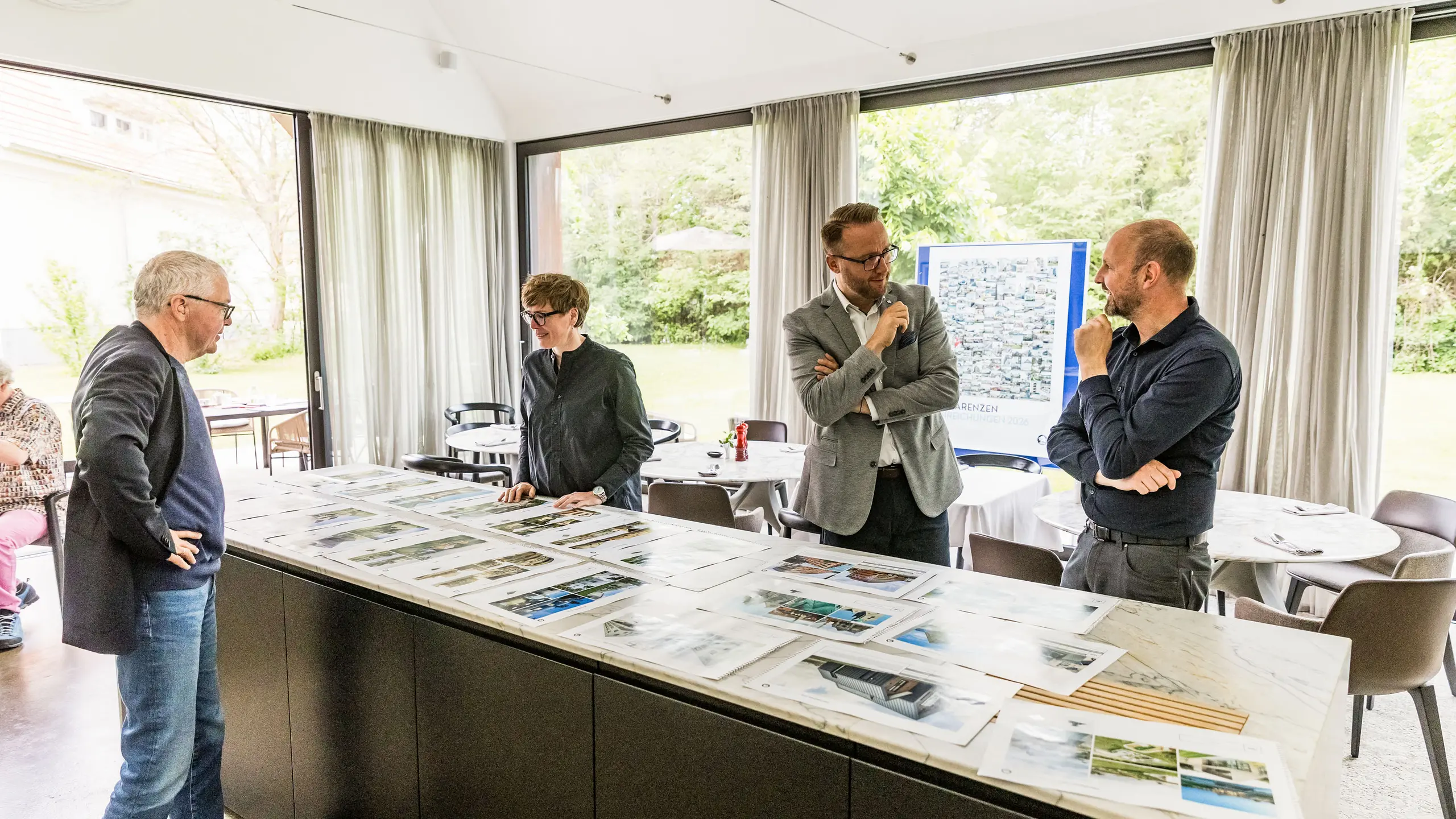 Konečný výběr architektonických vrcholů PREFARENZEN pro rok 2026 je prezentován porotě složené z významných členů na velkoformátových fotografiích. Odborníci pečlivě posuzují přihlášené architektonické projekty z hlediska jejich inovativní síly, kvality designu a použití materiálů PREFA. Setkání ve prosvětleném vinařském sídle v burgenlandském regionu Seewinkel představuje závěr intenzivního procesu hodnocení poroty pro Architektonickou knihu a kalendář PREFARENZEN 2026.