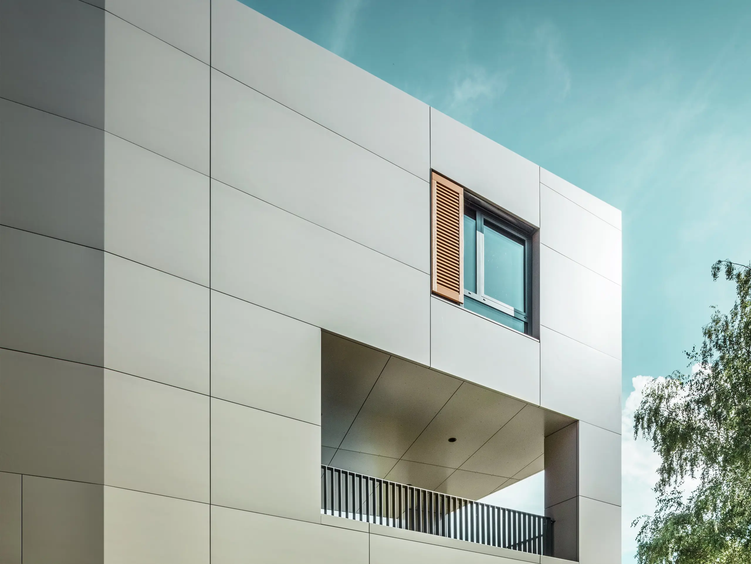 Obrázek ukazuje moderní radnici v Alzenau s fasádou z bronzových hliníkových kompozitních panelů od společnosti PREFA. Architektura se vyznačuje jasnými geometrickými tvary a velkými okny. Špičatá střecha a decentní osvětlení dodávají budově elegantní a moderní vzhled.