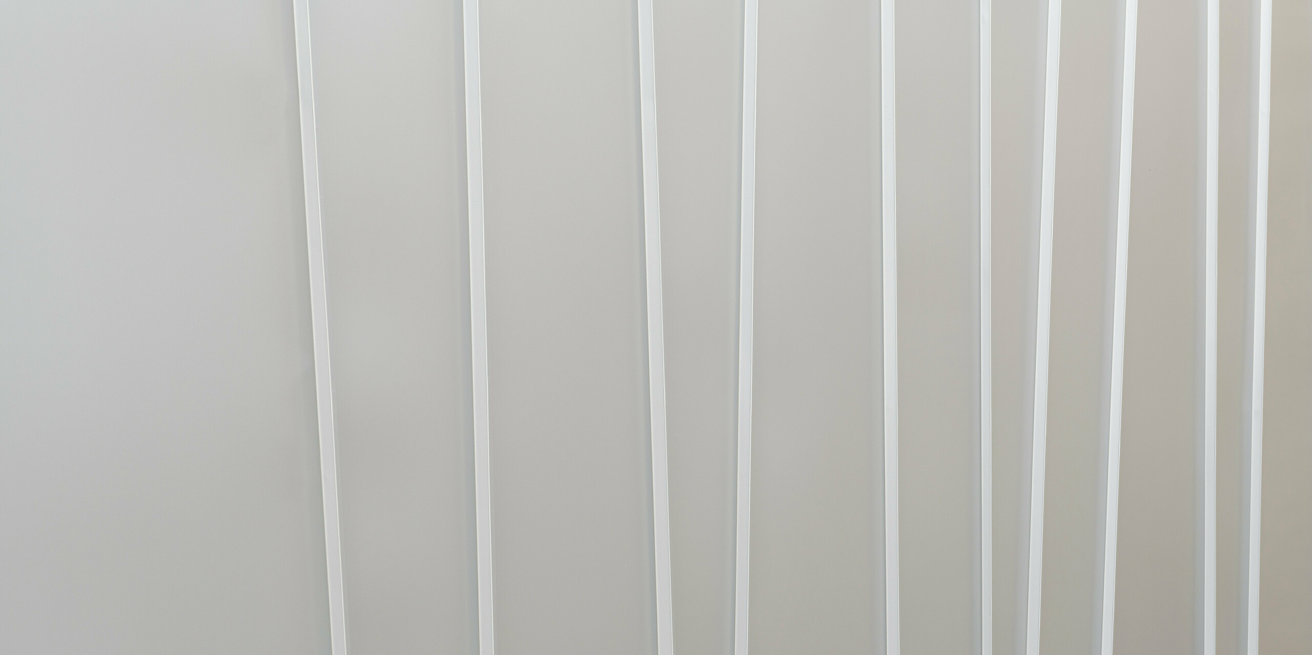 Detailní záběr na moderní fasádní systém z PREFALZ v barvě P.10 světle šedé barvě v různých šířkách pásů. Čistá a minimalistická textura navozuje pocit pořádku a současného designu.