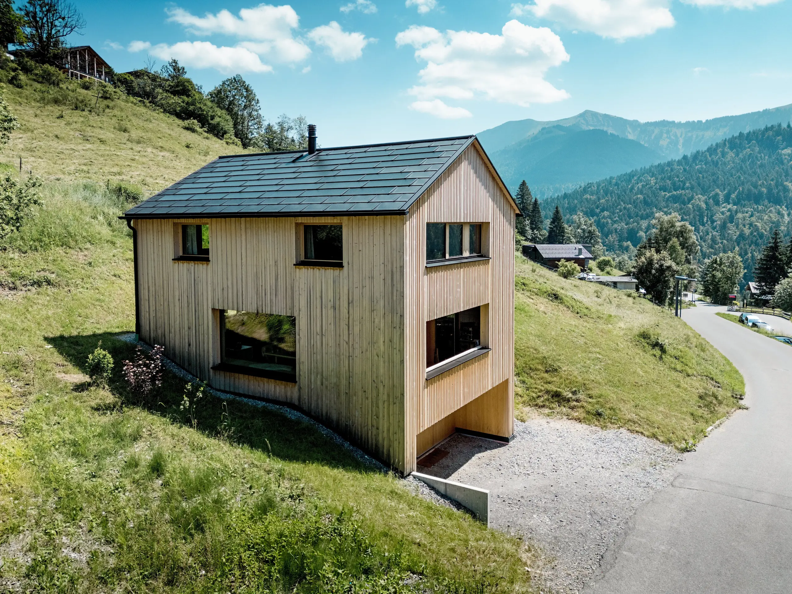 Vysoko nad údolím se na slunném svahu hory Ebnit tyčí dům Haus Immi jako drsný dřevěný monolit. Minimalistická fasáda z bílé jedle a černá solární střecha PREFA vytvářejí výrazný kontrast k rozlehlé alpské krajině. Integrované solární střešní panely a střešní panely R.16 v černé barvě P.10 vyrábějí solární energii, odolávají alpskému počasí a zajišťují dlouhodobý a harmonický vzhled střechy.