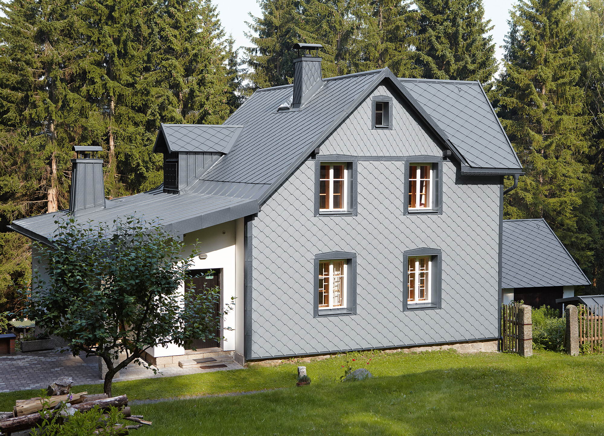 Fasáda s PREFA fasádní šablony 29 x 29 ve světle šedé barvě na návětrné straně Rodinný dům v lese s PREFA hliníkovou fasádou ve světle šedé odolnou vůči počasí.
