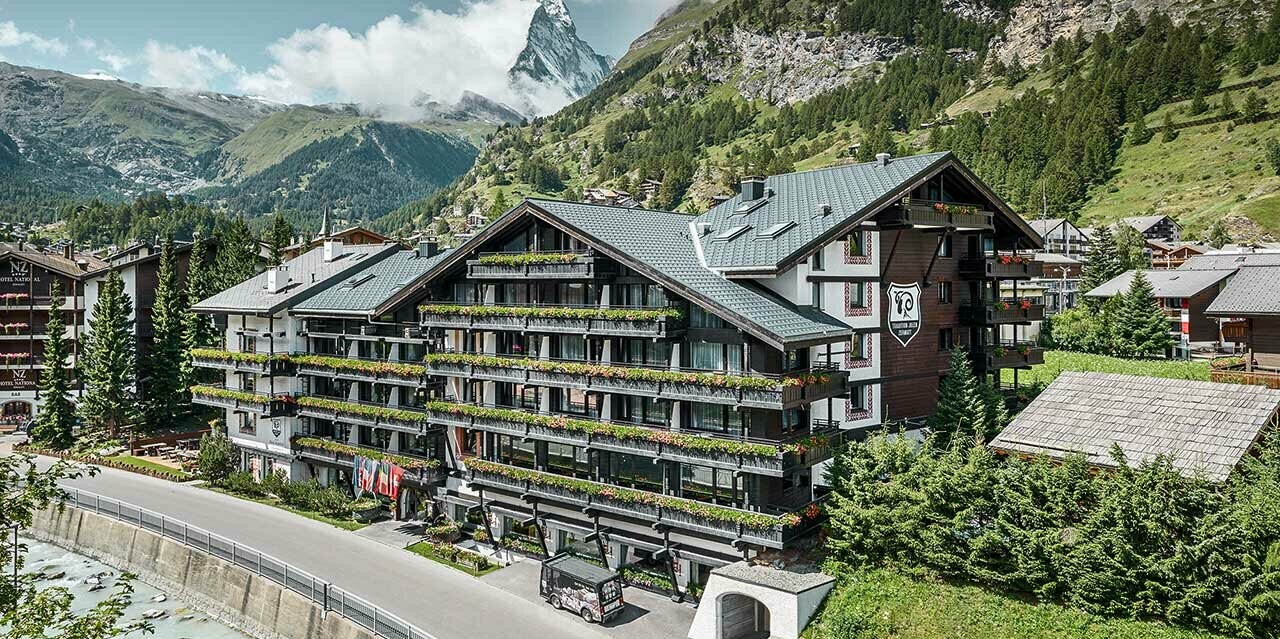 Hotel Alpenhof v Zermattu s Matterhornem v pozadí, balkony s tmavou dřevěnou fasádou a hliníkovou střechou PREFA antracitové barvě
