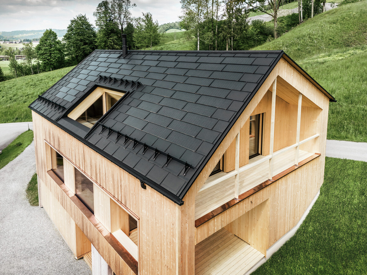 Rodinný dům v rakouském městě Egg s integrovaným solárním panelem PREFA a střešním panelem R.16 v barvě P.10 černé v kombinaci s dřevěnou fasádou