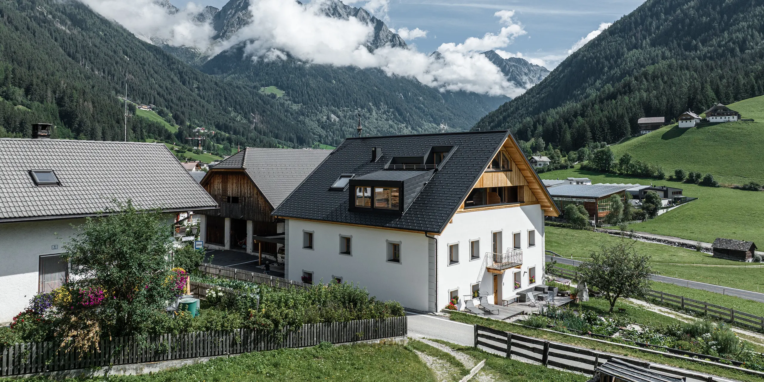 Pohled na prázdninové apartmány Ausserwegerhof v údolí Antholz, Jižní Tyrolsko, před působivou horskou kulisou. Objekt je charakterizován střechou PREFA se střešním šindelem v antracitové barvě DS.19. Hliníková sedlová střecha harmonicky zapadá do okolní přírody.