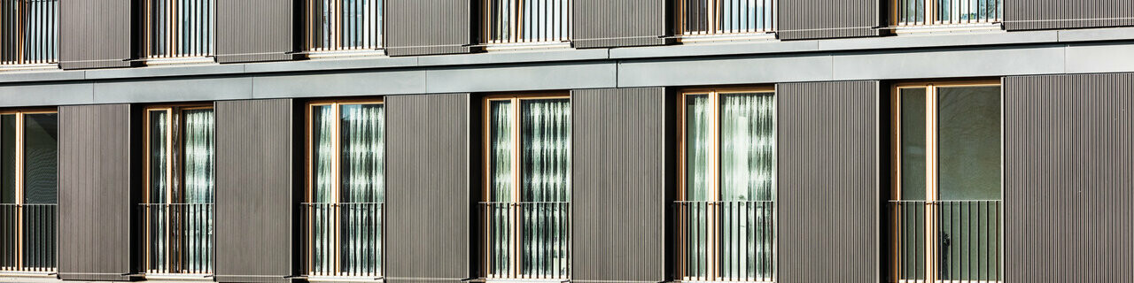 Čelní pohled na budovu s detailním pohledem na vlnitou hliníkovou fasádu z Profilwelle od PREFA v černošedé barvě.