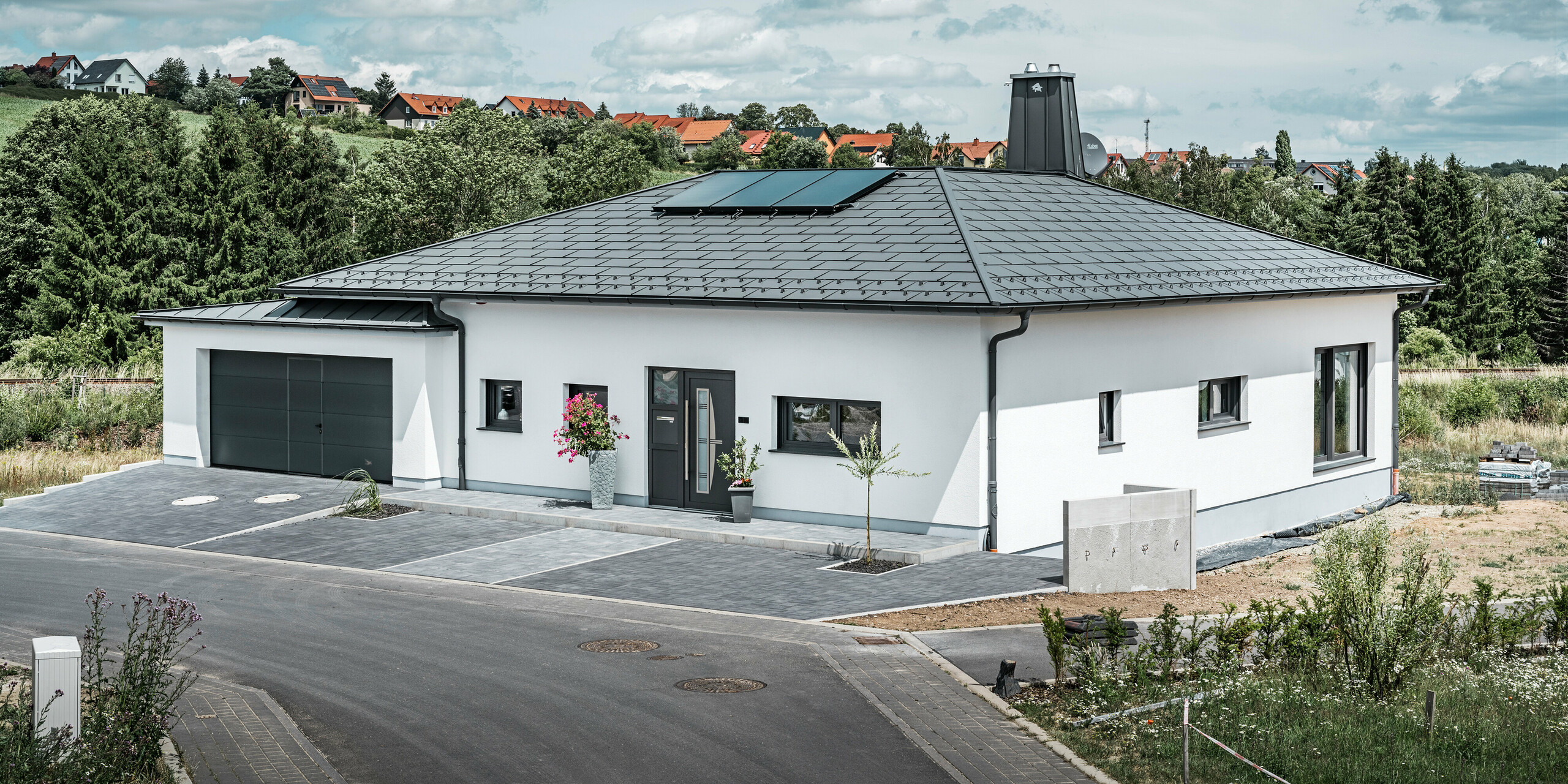 Přízemní dům s bílou omítkovou fasádou a tmavě šedou hliníkovou střechou od PREFA