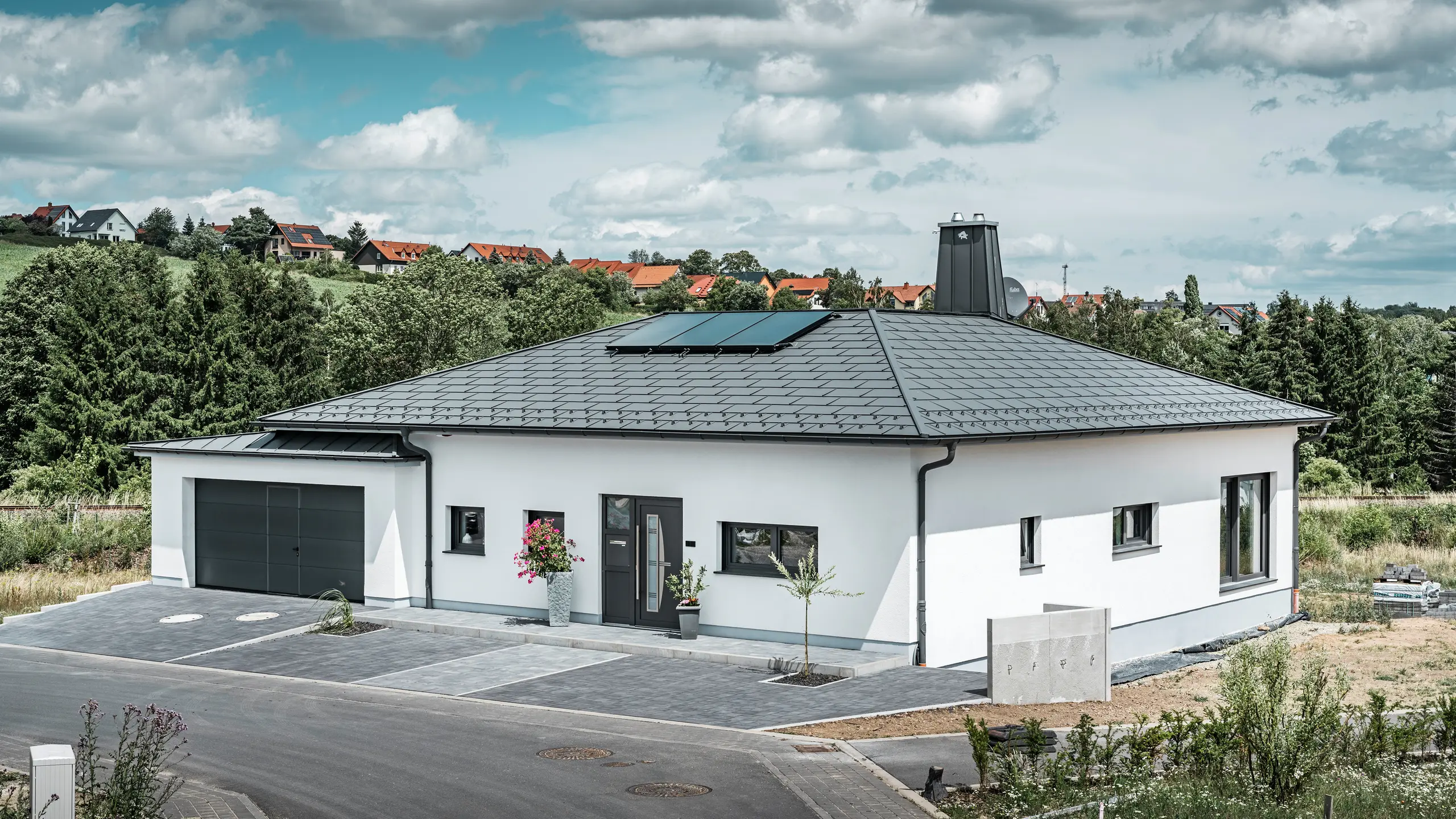Přízemní dům s bílou omítkovou fasádou a tmavě šedou hliníkovou střechou od PREFA