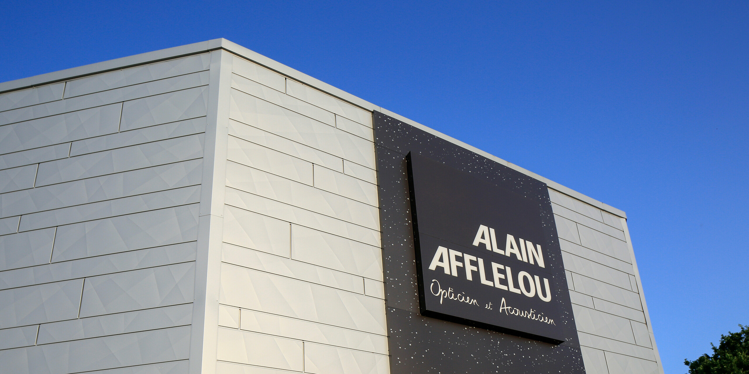 Vstupní prostor prodejny AFFLELOU v Auray s velkým firemním nápisem a extravagantní fasádou z PREFA Siding.X ve stříbrné metalíze