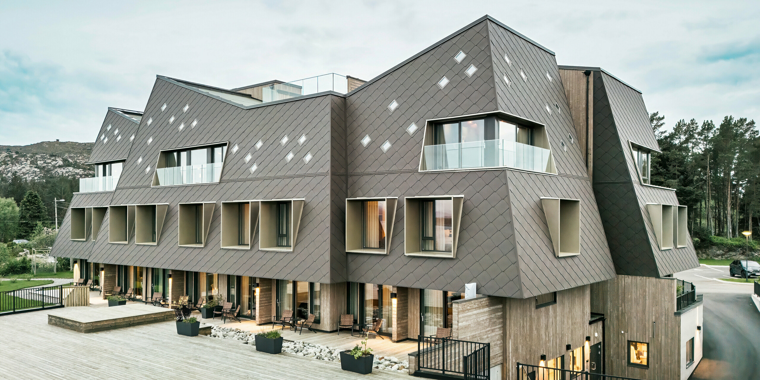 Pohled na terasu hotelu Beckerwyc House v Bekkjarviku, Norsko. Moderni budovu zdobí nápadná hliníková fasáda z PREFA fasádních šablon 44 × 44 v oříškové barvě. Přírodní barevnost fasády harmonicky zapadá do okolní krajiny a podtrhuje zajímavý design budovy.