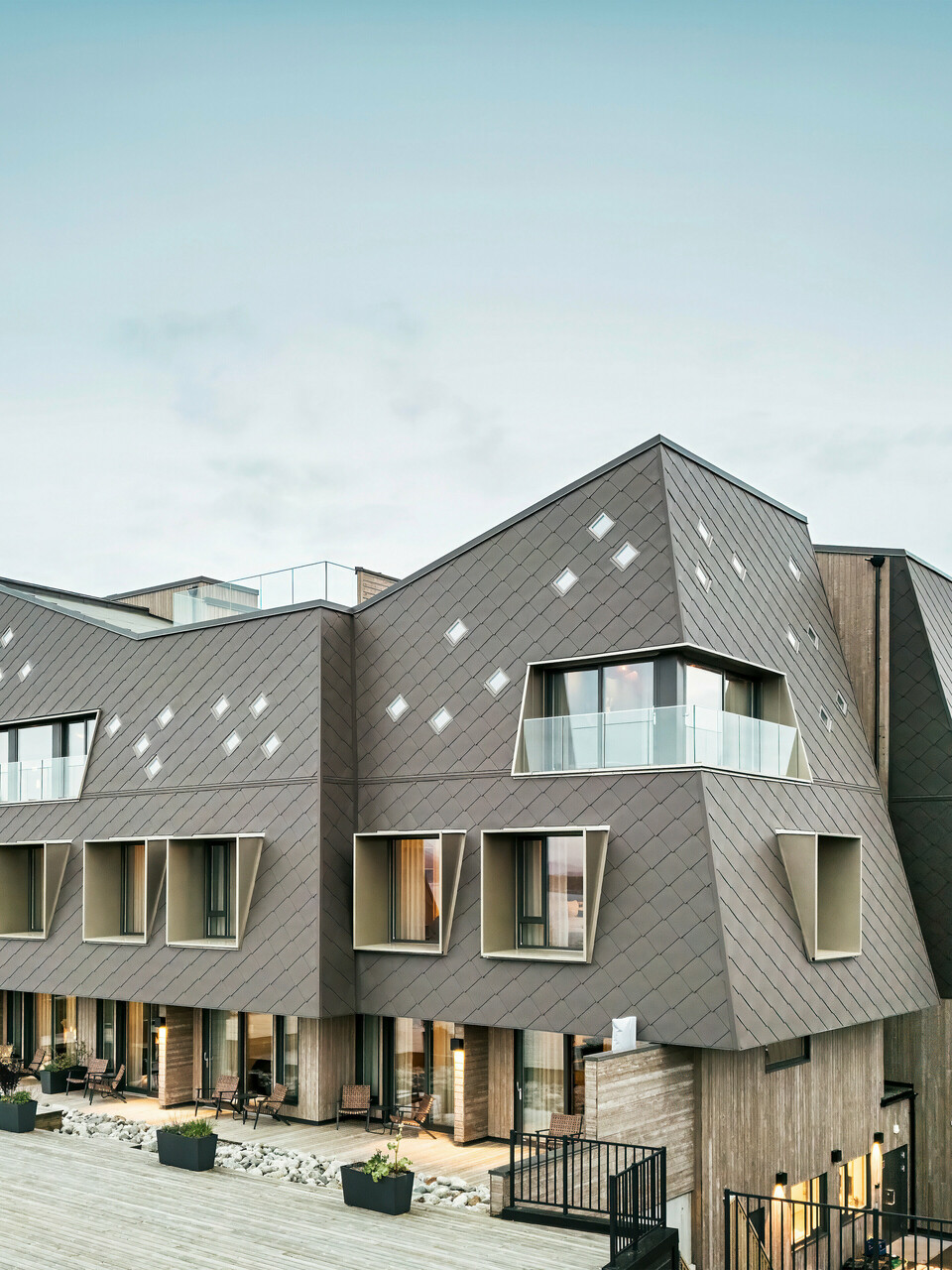 Pohled na terasu hotelu Beckerwyc House v Bekkjarviku, Norsko. Moderni budovu zdobí nápadná hliníková fasáda z PREFA fasádních šablon 44 × 44 v oříškové barvě. Přírodní barevnost fasády harmonicky zapadá do okolní krajiny a podtrhuje zajímavý design budovy.