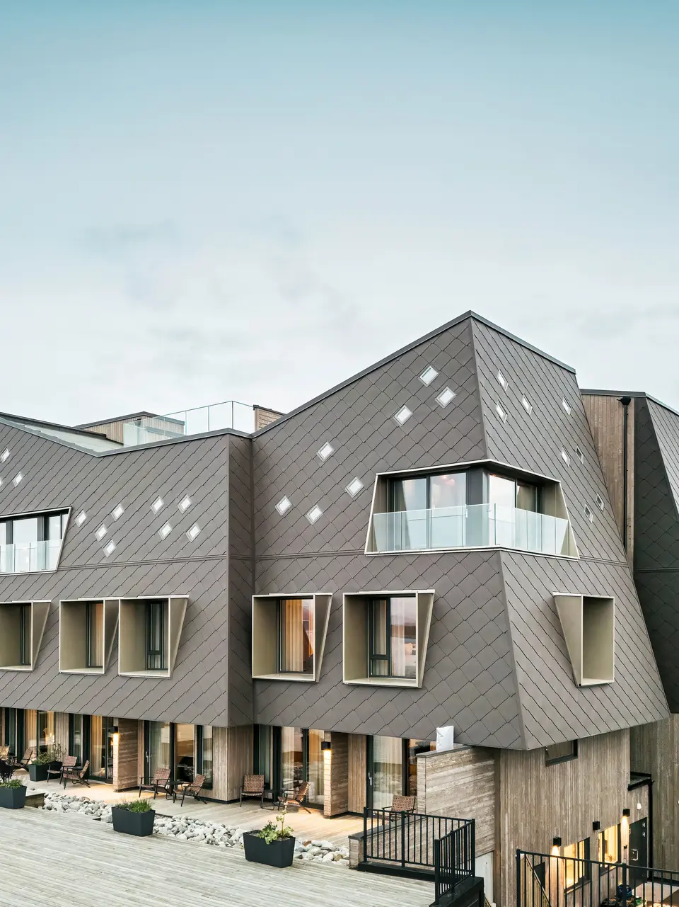 Pohled na terasu hotelu Beckerwyc House v Bekkjarviku, Norsko. Moderni budovu zdobí nápadná hliníková fasáda z PREFA fasádních šablon 44 × 44 v oříškové barvě. Přírodní barevnost fasády harmonicky zapadá do okolní krajiny a podtrhuje zajímavý design budovy.