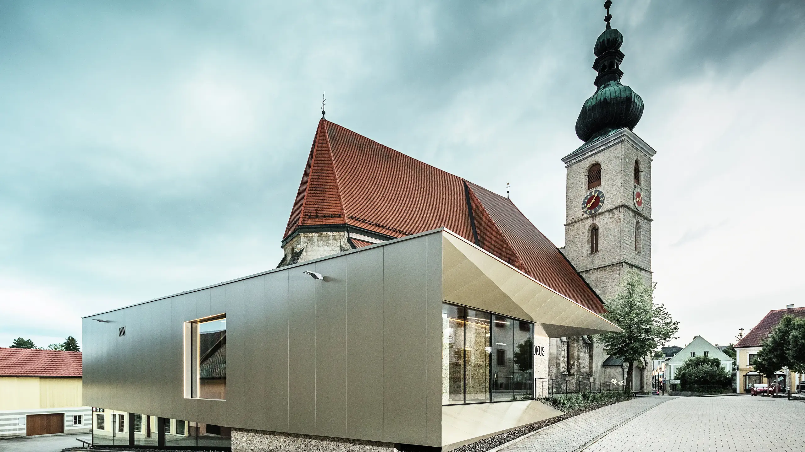 Boční pohled ukazuje filigránový přesah střechy, realizovaný pomocí vysoce kvalitních hliníkových kompozitních desek PREFA. Precizní zpracování umožňuje moderní vzhled s čistými liniemi a podtrhuje architektonické propojení starého a nového.