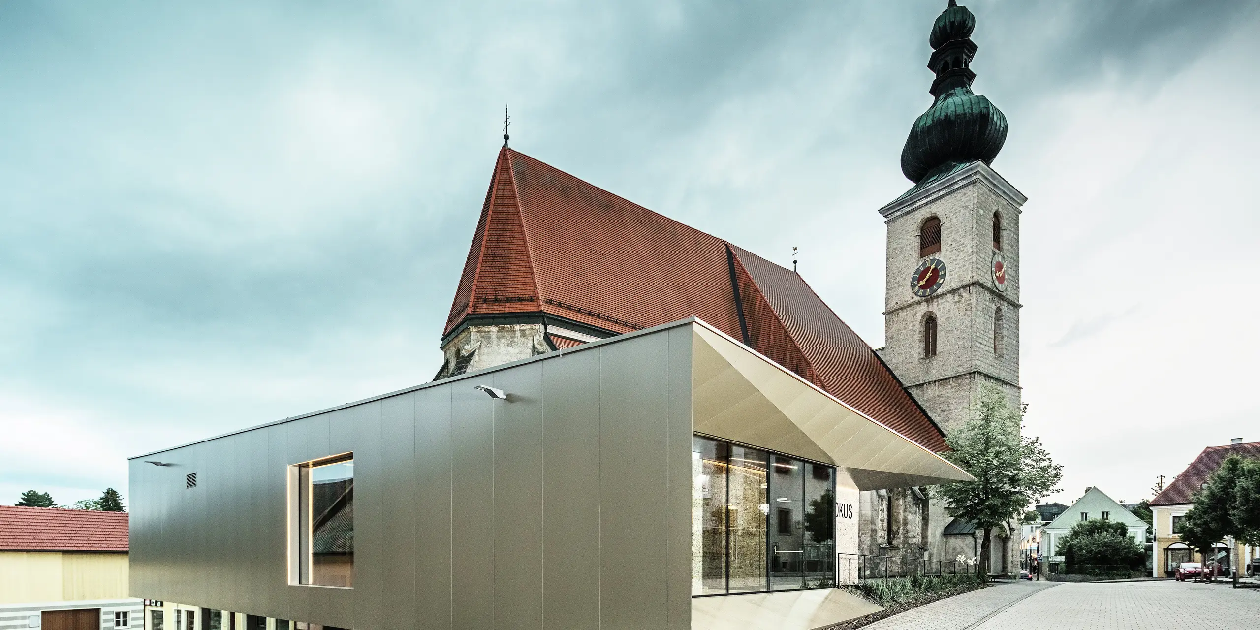 Boční pohled ukazuje filigránový přesah střechy, realizovaný pomocí vysoce kvalitních hliníkových kompozitních desek PREFA. Precizní zpracování umožňuje moderní vzhled s čistými liniemi a podtrhuje architektonické propojení starého a nového.