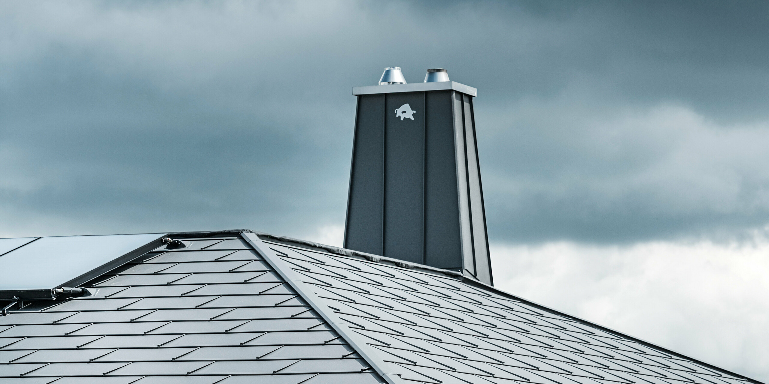Pohled na střechu s oplechovaným komínem z plechu PREFALZ a nalepeným býkem - logo firmy PREFA