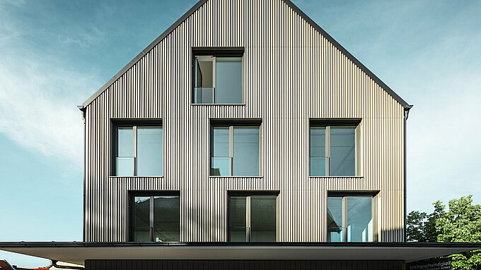 Na obrázku je moderní budova ve Feldkirchu, kterou navrhl architekt Stefan Heigl. Fasáda je obložena Prefalz v barvě bronzu, sedlová střecha je pokryta Prefalz v černo-šedé. Velká, obdélníková okna poskytují dostatek přirozeného světla uvnitř. Budova kombinuje vysoce kvalitní materiály a elegantní architekturu, která je funkční i esteticky příjemná. Tato moderní konstrukce a použití materiálů Prefalz dodávají budově současný a stylový vzhled.