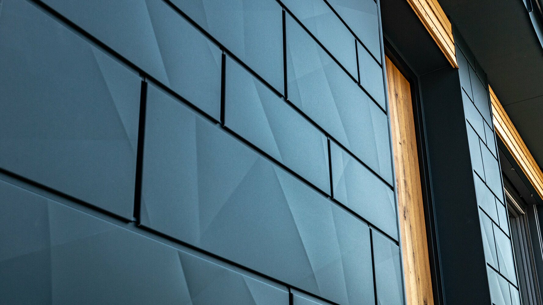 Fasádní panely PREFA v lomeném vzhledu; hliníkový fasádní systém PREFA Siding.X v antracitové barvě doplněný dřevěnou fasádou.